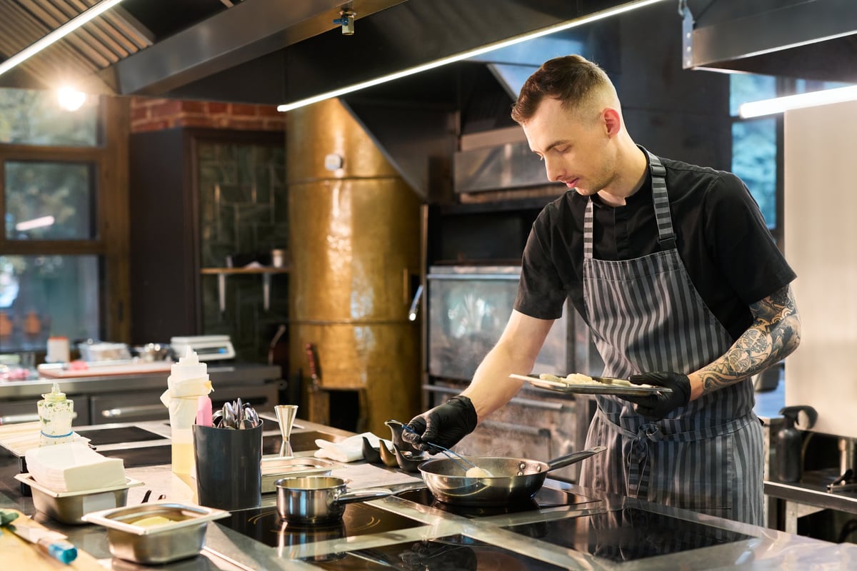 Young cook in an apron and gloves preparing food in a professional kitchen