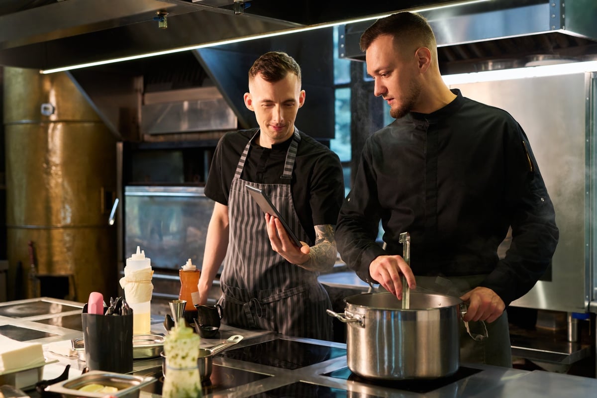 Two cooks working together in a professional kitchen with a tablet