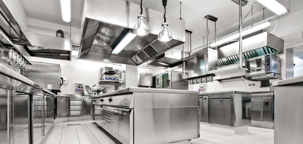 Spacious commercial kitchen with ovens, stoves, prep counters and ventilation hoods